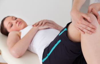 A doctor examining injured knee of a young woman athlete.